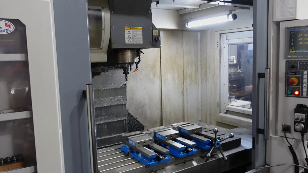 CNC vertical machining center with Kurt vises and the C&M logo on the door, inside the C&M shop