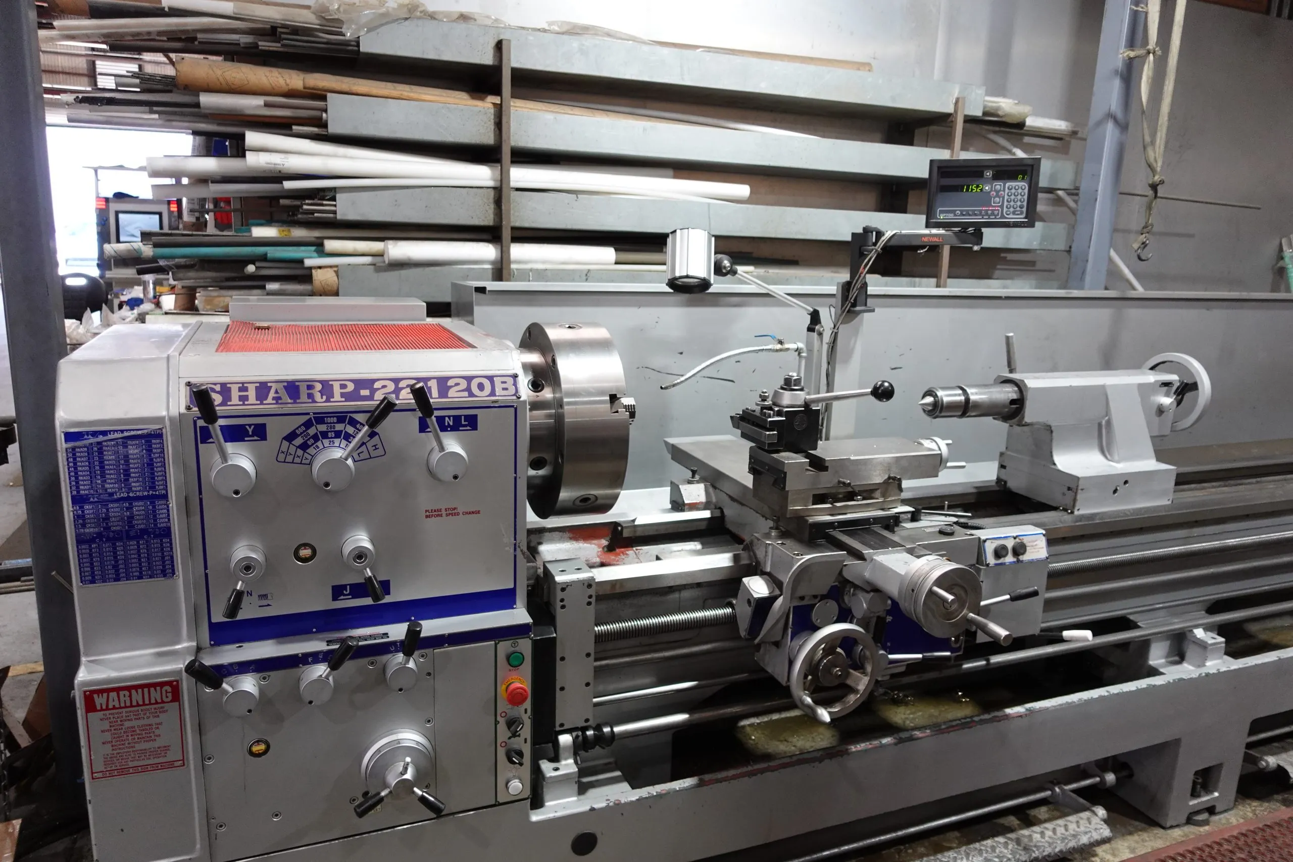 Long lathe bed with a chuck, a tailstock and a digital readout, bar stock racked behind